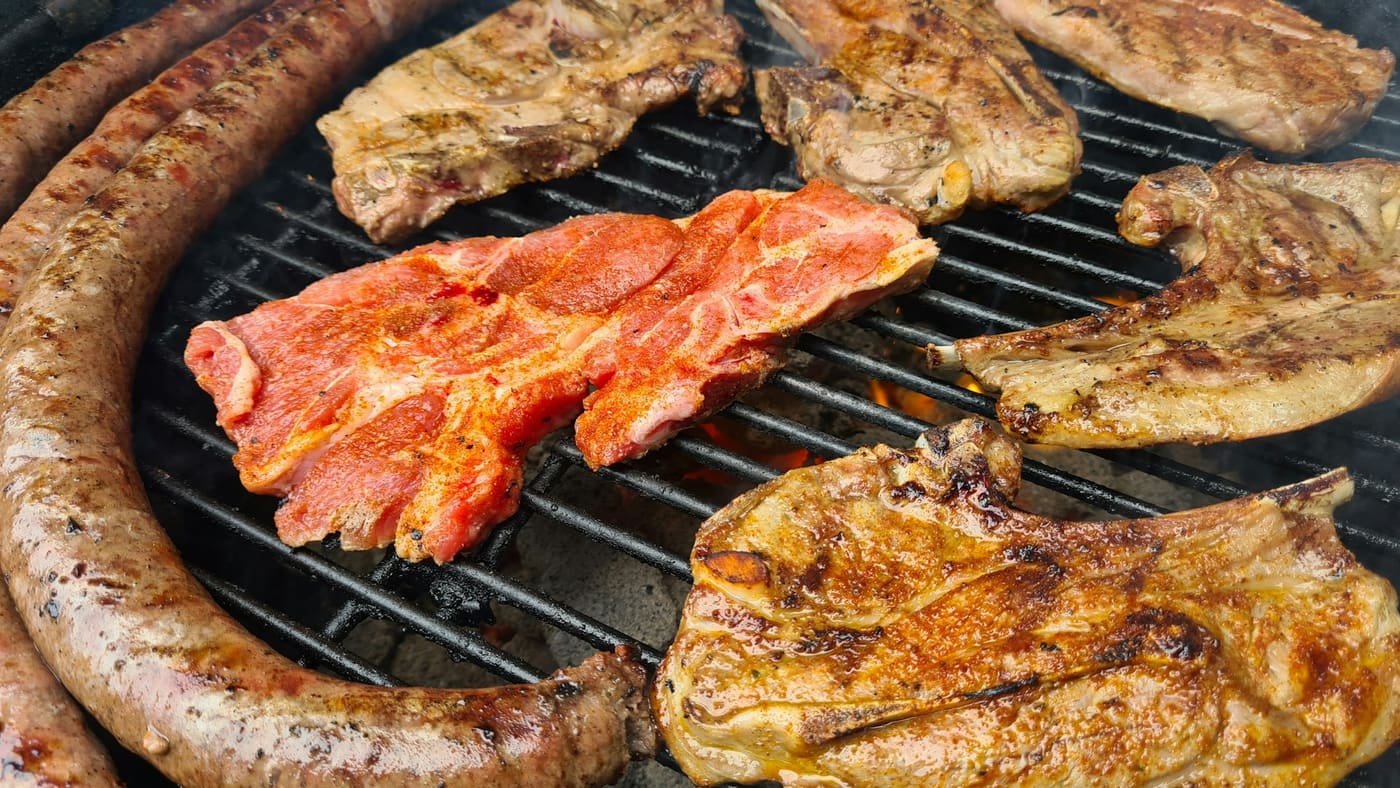 Boerewors, lamb chops, and ribs cooking over coals on an open braai